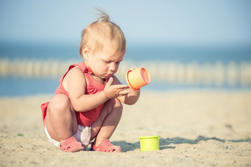 Baby playing on the sandy beach near the sea. Cute little girl in red dress with sand on tropical beach. Ocean coast.