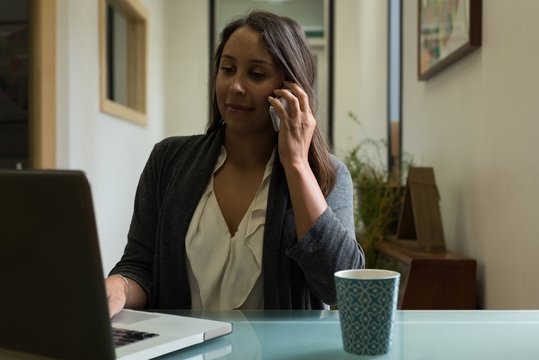 Female executive using mobile phone while talking on mobile