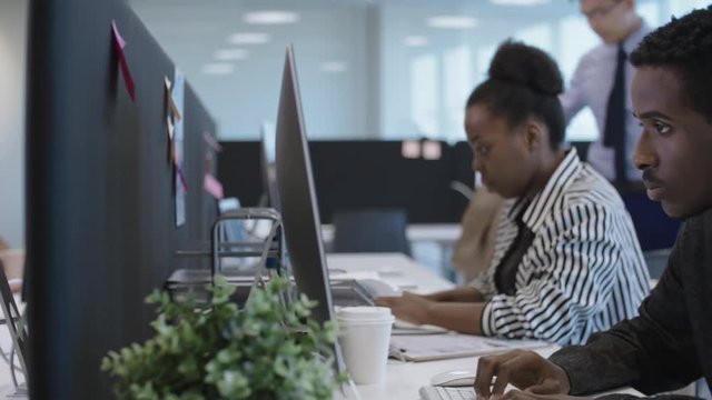 Tracking of open space office with businessmen and businesswomen of mixed ethnicities working on computers at desks