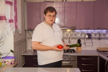 A fat man with a beer belly in a lilac kitchen. Healthy food. Big Man and healthy vegetables