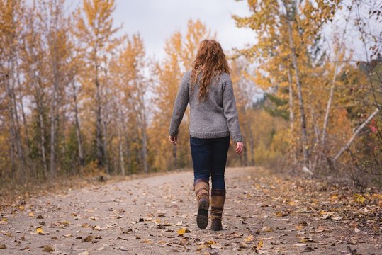 Red head woman walking on the path through autumn forest