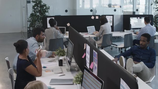 High angle of excited multi-ethnic colleagues having fun in open space office: men and women throwing crumpled paper balls to each other and laughing
