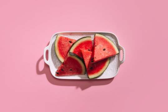 Fresh sliced watermelon in white dish on pink background.