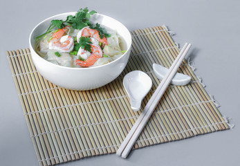 Shrimp Wonton and prawn hot soup in white bowl and white chopsticks on bamboo grille and gray table background. Chinese New Year favorite food.