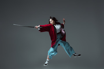 Fototapeta na wymiar samurai in kimono fighting with katana in jump isolated on grey