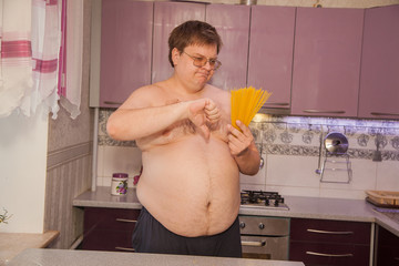 A fat man with a beer belly in a lilac kitchen. Junk food. Pasta