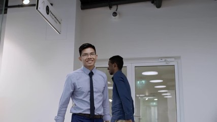 Young Asian businessman walking into office, shaking hands with African colleague, smiling and walking to workplace