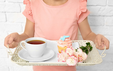 Little girl holding tray with breakfast and flowers for her mommy on Mother's Day against brick wall