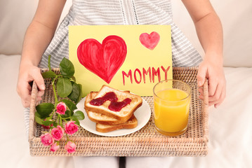 Obraz na płótnie Canvas Little girl holding tray with breakfast and greeting card for her mommy on Mother's Day indoors