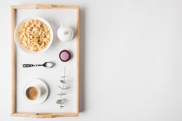 top view of breakfast with cork flakes in bowl and cup of coffee on tray on white surface