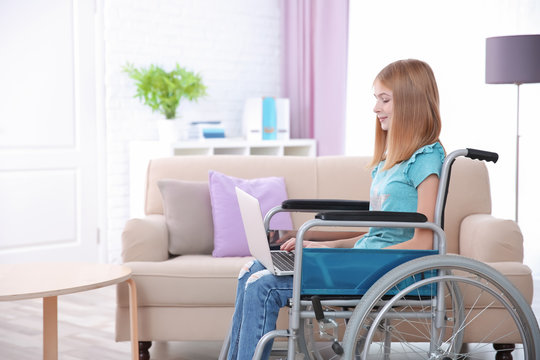 Teenage girl in wheelchair using laptop indoors