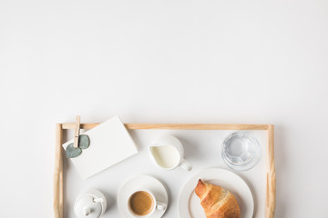 flat lay with cup coffee and croissant for breakfast on tray on white tabletop