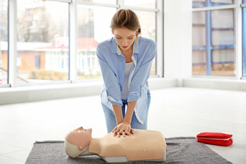 Young woman practicing first aid on mannequin indoors