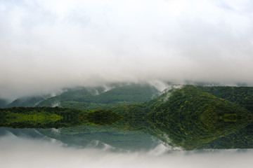 Morning mist over wooded hills and lake, forest reflected on cold water