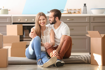 Young couple with moving boxes on floor in kitchen at new home