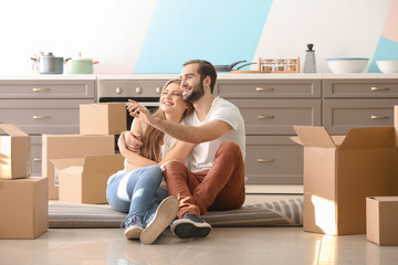 Young couple with moving boxes on floor in kitchen at new home