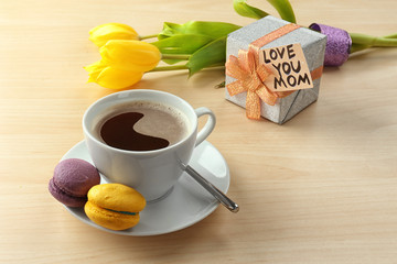 Tasty macarons, cup of coffee and gift box on table. Mother's day breakfast