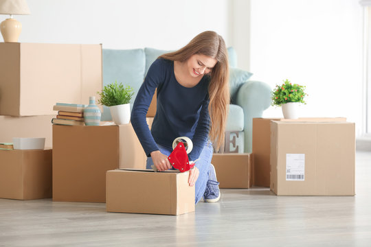 Young woman packing moving box in room at home