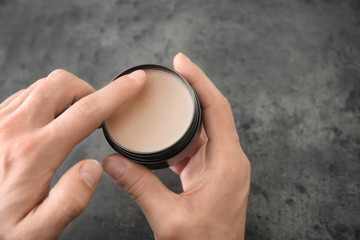 Male hands with jar of clay for hair on grey background, closeup