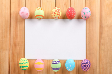 Decorated Easter eggs and blank sheet of paper on wooden background