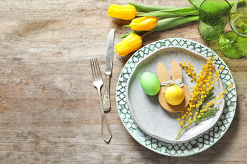 Beautiful festive Easter table setting with painted eggs and mimosa on wooden background
