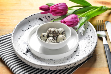 Beautiful festive Easter table setting with quail eggs and tulips on wooden background