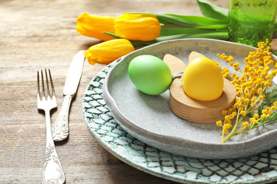 Beautiful festive Easter table setting with painted eggs and mimosa, closeup