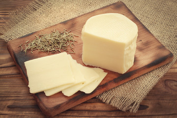 Suluguni cheese sliced on wooden plate with dried rosemary condiment