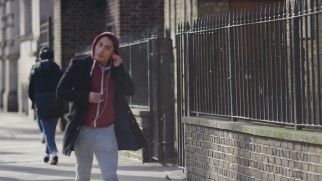 Young casually dressed man puts his earphones in his ears whilst walking, in slow motion