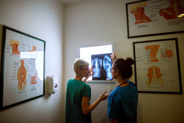 Rear view of two professional nurses checking X-ray and consulting in a doctors office.
