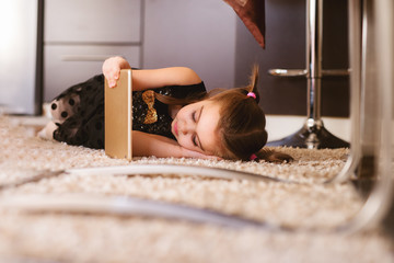 Portrait of little toddler child girl lying on a carpet on the side while holding a tablet.