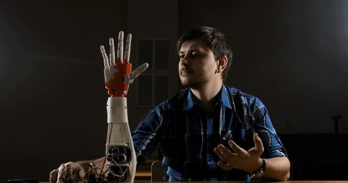 Man creates movement for mechanical plastic arm. Cybernetic robotic arm. Robots arm movement. Futuristic made on 3D printer device.
