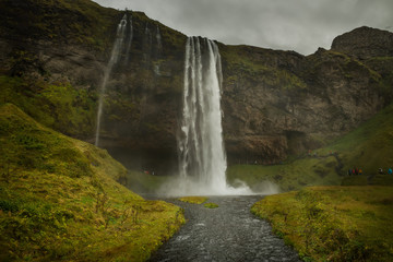 A powerful waterfall among the rocks covered with green moss. Iceland. Dark fabulous atmosphere, vintage.
