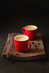 Two red cups of espresso on dark wooden background decorated coffee beans
