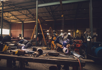 Welder in protective uniform and mask welding metal pipe on the industrial table while sparks...