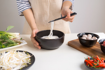 Female chef prepare traditional Vietnamese soup Pho bo with herbs, meat, rice noodles