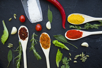 Cooking a hot spicy meal with a set of spices and herbs in wooden spoons, fresh rosemary, lettuce,...