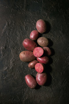 Raw uncooked organic potatoes named lilu rose, whole and slice over dark texture background. Top view, copy space