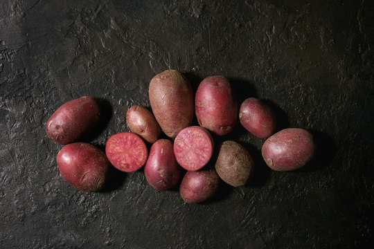 Raw uncooked organic potatoes named lilu rose, whole and slice over dark texture background. Top view, copy space
