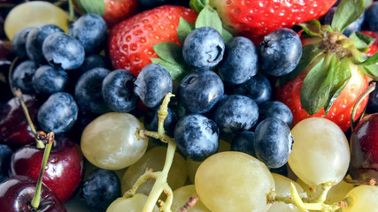 Mixed fruits large background. Variety fresh fruits: cherry, grapes, blueberry, strawberry. Healthy eating and raw diets concept.