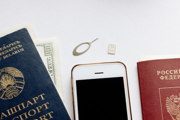 Russian and Belorussian passports, white smartphone, bank card, dollars money are isolated on the white background. Sim-card and clip