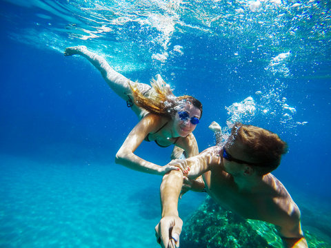Underwater selfie with a stick of young excited joyful love couple swimming and enjoying with goggles in the exotic turquoise sea at summer vacation or honeymoon.