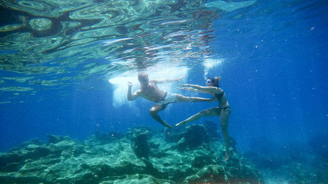 Underwater photo of young playful joyful love couple imitating fight scene with goggles in the exotic turquoise sea near the coral reef.