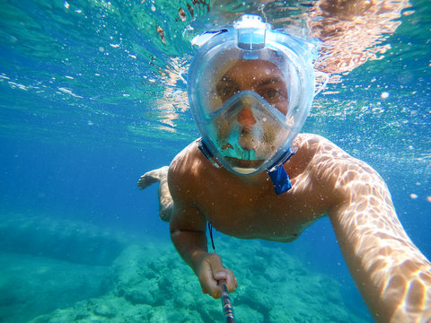 Underwater portrait photo of young muscular cheerful man exploring and enjoying with snorkelling mask in the exotic turquoise sea.