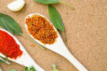 Two wooden spoons with dry spices and fresh herbs on a corkwood background with copy space, top view, close up