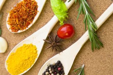Cooking hot spicy meal. A set of three different spices in wooden spoons, fresh cherry tomatoe, garlic and rosemary, corkwood background, top view