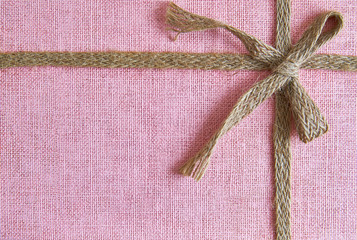 Pink background with burlap ribbon and bow. Top view with copy space