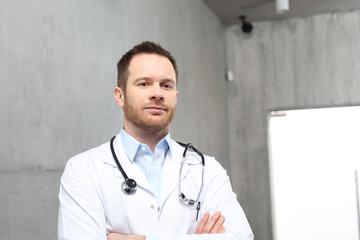 Lekarz. Przystojny lekarz ubrany w biały kitel stoi w klinice - obrazy, fototapety, plakaty