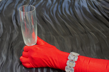 Hand with a red glove and necklace holding a cup on dark background