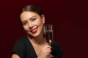 Closeup portrait of sensual brunette woman holding a glass of champagne, over red background